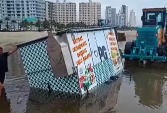 Trator é acionado para retirar carrinho de ambulante que atolou na areia da praia; VÍDEO